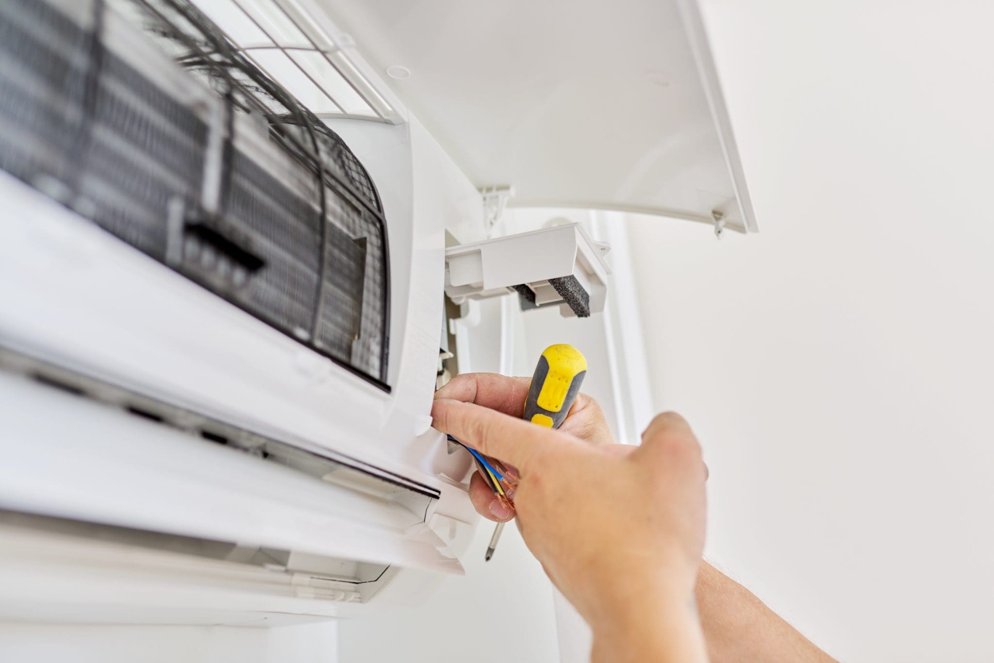Installing an air conditioner in an apartment office, close-up of an engineer installer's hand with an indoor unit, male technician repairing with a screwdriver